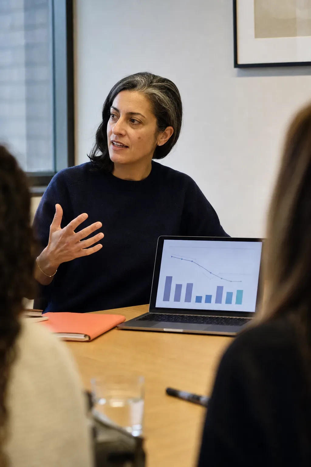 A CMO mid-presentation at a conference table, with an attribution dashboard visible on her laptop.
